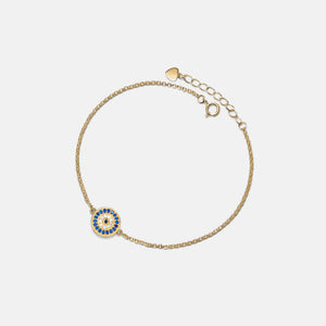 Gold bracelet with a blue and gold evil eye charm on a light gray background