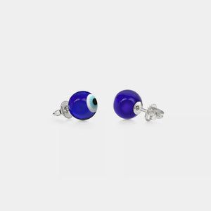 A pair of stud earrings featuring a blue 'evil eye' design on a white background