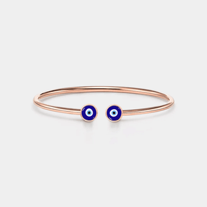 A gold-plated sterling silver bangle bracelet with two blue enamel evil eye charms on the front.