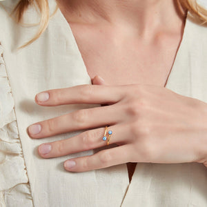Woman wearing a ring with blue evil eye charms on a light gray background