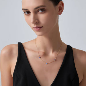 Woman wearing a delicate necklace with small blue beads against a plain background