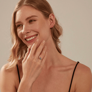 Woman wearing a silver chain ring with a blue evil eye charm on a beige background