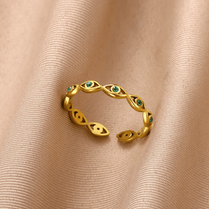 Gold evil eye ring with green gemstones on a beige fabric background