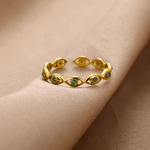 Gold evil eye ring with green gemstones on a beige background