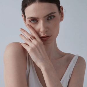 Woman wearing a gold three row ring with blue evil eye charms on a light gray background