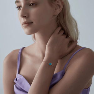 Woman wearing a gold locket bracelet with a turquoise stone on a light gray background