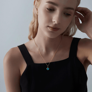 A woman wearing a gold necklace with a turquoise locket on a light gray background