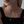 A woman wearing a gold necklace with a turquoise locket on a light gray background
