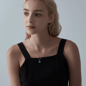 A woman wearing a gold necklace with a turquoise locket on a light gray background