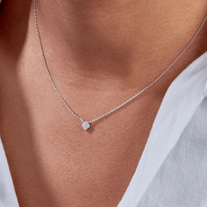 Necklace with a heart-shaped pendant worn by a person wearing a white shirt.