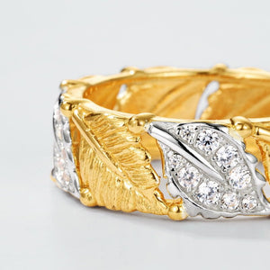 Gold and silver ring with leaf design and diamond accents on a light gray background