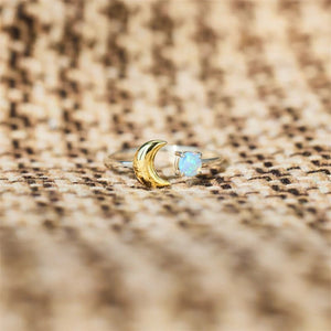Gold ring with a moon design and opal stone on a beige fabric background