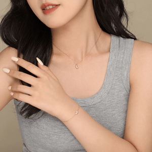 Woman wearing a gold necklace and bracelet against a neutral background