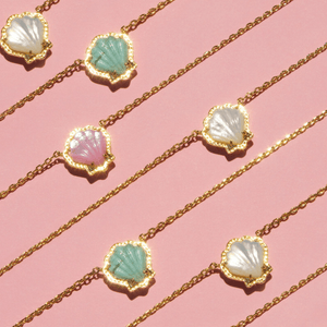 Gold necklaces with shell-shaped pendants on a pink background