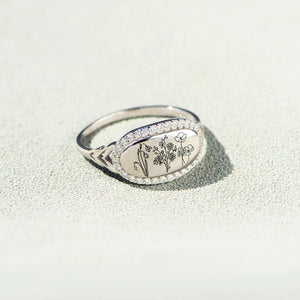 A silver ring with a floral design and what appears to be gold plating on the band, displayed against a neutral background.