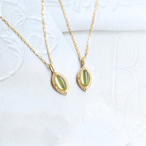 Two gold necklaces with green gemstones on a white textured background