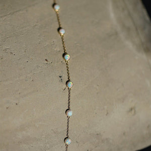 Gold chain necklace with opal beads on a textured surface