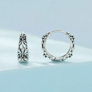 A pair of vintage style silver earrings with purple iris flower design, placed on a light blue surface.