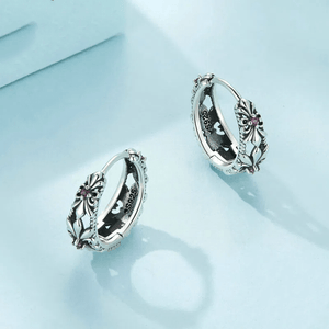 A pair of vintage style silver earrings with purple iris flower design, placed on a light blue surface.