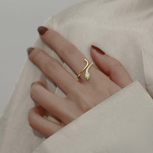 Model wearing a gold snake-shaped ring with gemstones on a gray background