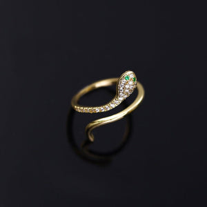 A gold-colored bypass ring with a snake design, featuring cubic zirconia, displayed on a black background.