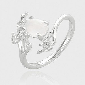Silver ring with floral designs and a central gemstone on a light gray background