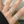 Silver ring with a central gemstone on a finger, with a blurred background.