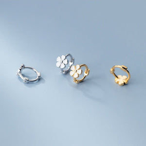 Set of three floral-shaped earrings in silver, gold, and rose gold on a light blue background.