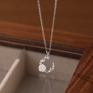 Silver necklace with a floral pendant on a reflective surface