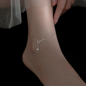Silver anklet on a person's ankle against a dark background