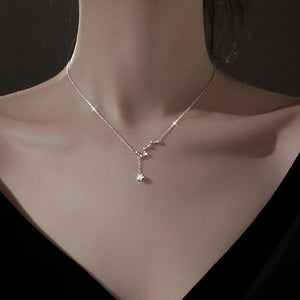 Silver necklace with a star-shaped pendant on a person's neck against a dark background