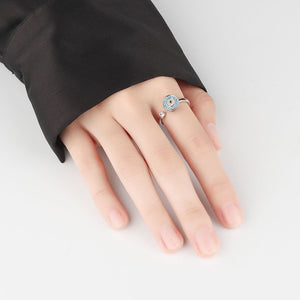 Woman wearing a silver evil eye spinner ring with blue gemstones and a diamond on a white background