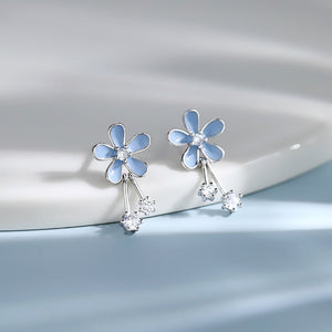 Flower-shaped earrings with blue petals and clear stones on a light gray background