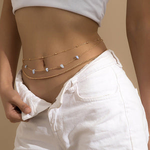 Person wearing a gold chain belt with small stones on a beige background