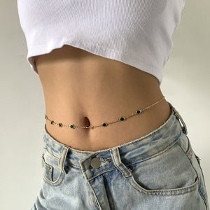 Person wearing a gold chain belt with green stones on a neutral background