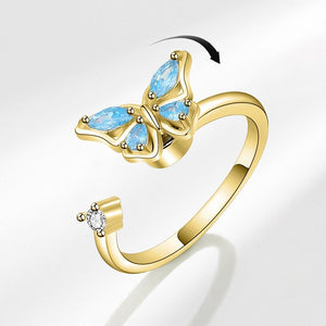 A gold-colored butterfly-shaped fidget spinner ring with blue cubic zirconia accents on a white background.