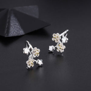 Silver floral earrings with gold accents on a dark background