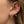 Gold ear stack featuring heart-shaped stud and drop earrings with pink and iridescent stones, including dangling bear charm details, styled on a model’s ear.
