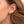 Gold ear stack featuring colorful charm drop earrings with cloud designs, dangling chains, and blue gemstone accents, styled on a model’s ear with multiple piercings.