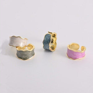 Three gold-rimmed rings with different colored centers on a light gray background