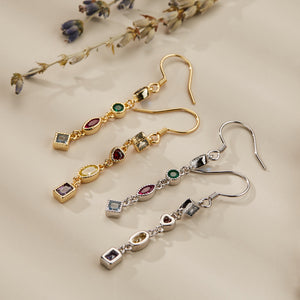 A set of three pairs of drop earrings, each featuring a series of multicolored gemstones with gold and silver accents, displayed on a beige background with dried lavender.