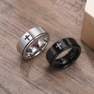 Two rings, one silver and one black, with cross designs on a wooden surface.