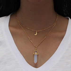 Gold necklaces with a moon pendant and a clear stone pendant on a white shirt.