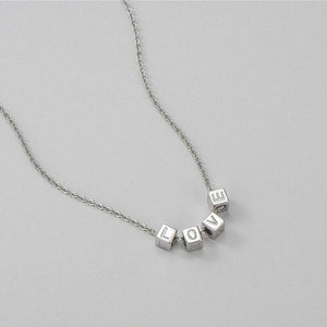 Silver necklace with cube beads spelling 'LOVE' on a light gray background