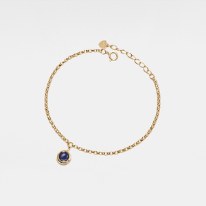 Gold bracelet with a blue gemstone on a light gray background