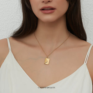 A model wearing a gold locket necklace with letter and envelope charm on a white background