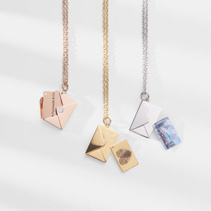 Three locket necklaces with letter and envelope charms on a white background
