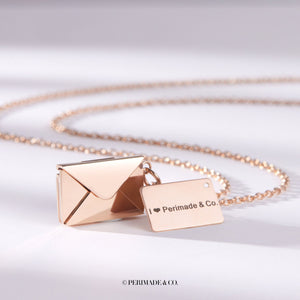 Rose gold locket necklace with letter and envelope charm on a white background