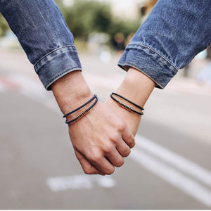 Two hands holding each other with bracelets on, wearing rolled-up jeans.