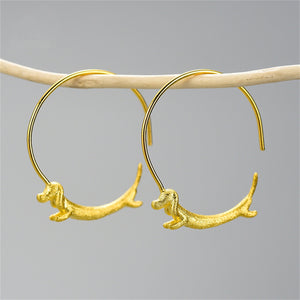 Gold hoop earrings with dog figures on a gray background